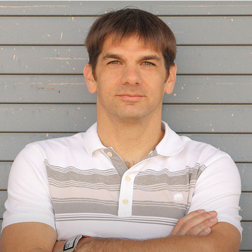Kevin Keller wearing a white and gray striped polo, contently looking at the camera with arms folded.