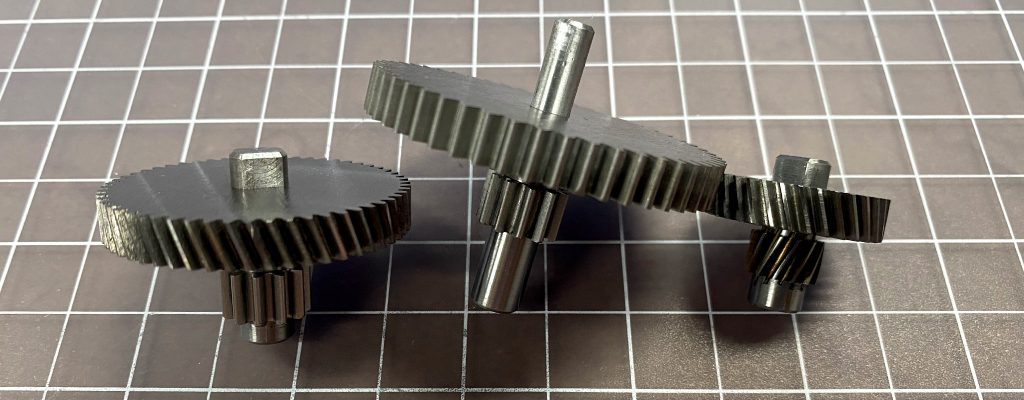 Three gears in different sizes, sitting on a cutting mat.