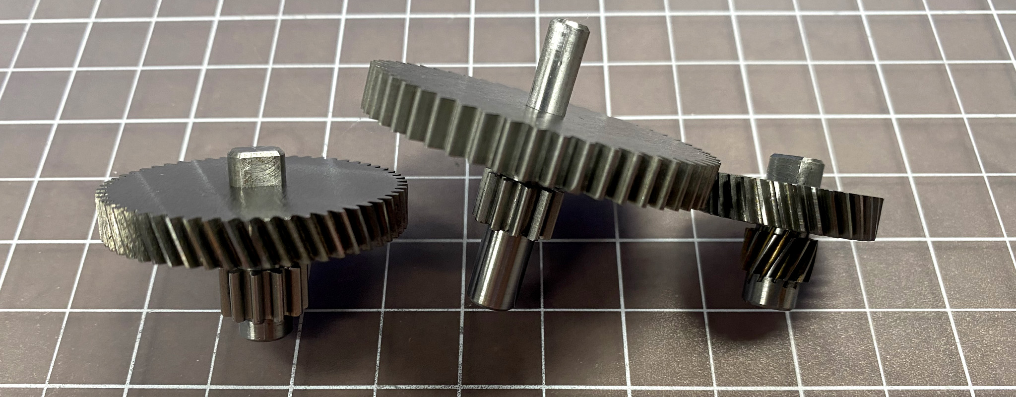 Three gears in different sizes, sitting on a cutting mat.