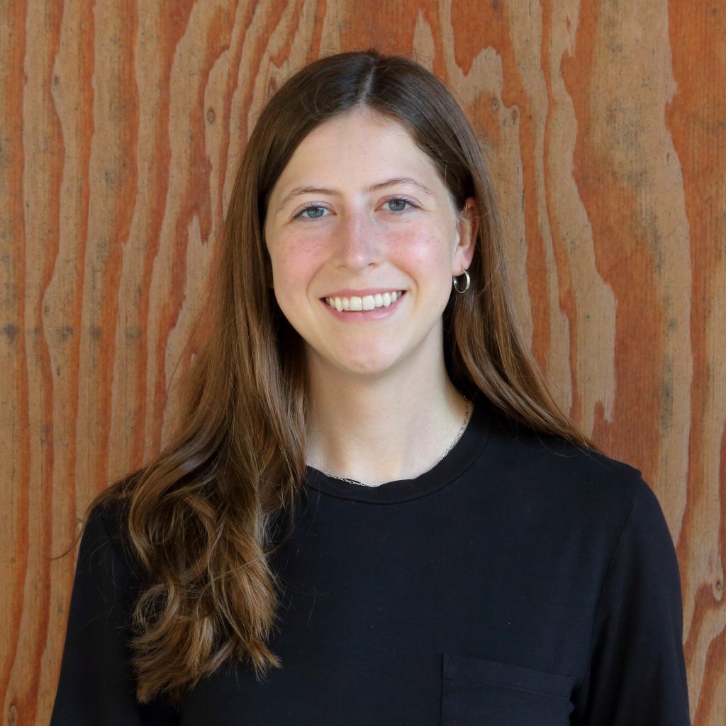 Melisa Cosler smiling standing in front of a wooden wall.