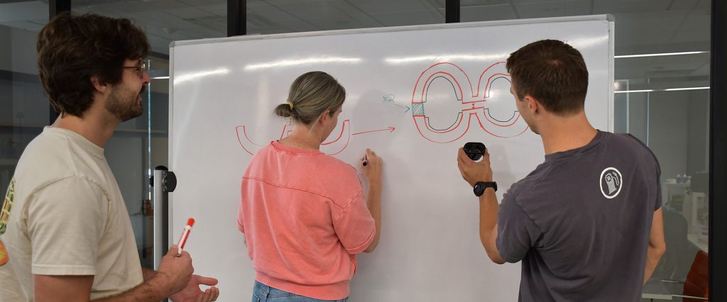 Liz, Jack and Greg standing in front of a whiteboard with a prototype and a drawing of the prototype.