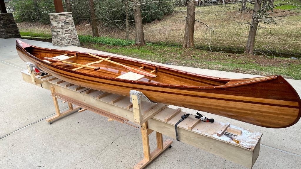 A glossed finished canoe on the making boards overtop a concrete parking spot.
