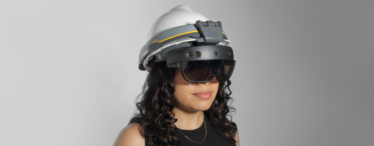 A woman in black wearing the Trimble XR10 attached to a white hard hat with the HoloTint attached.