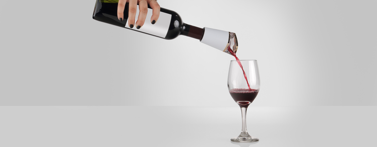 The PureWine Phoenix attached to a dark wine bottle with a hand holding the bottle pouring the red liquid into a wine glass.
