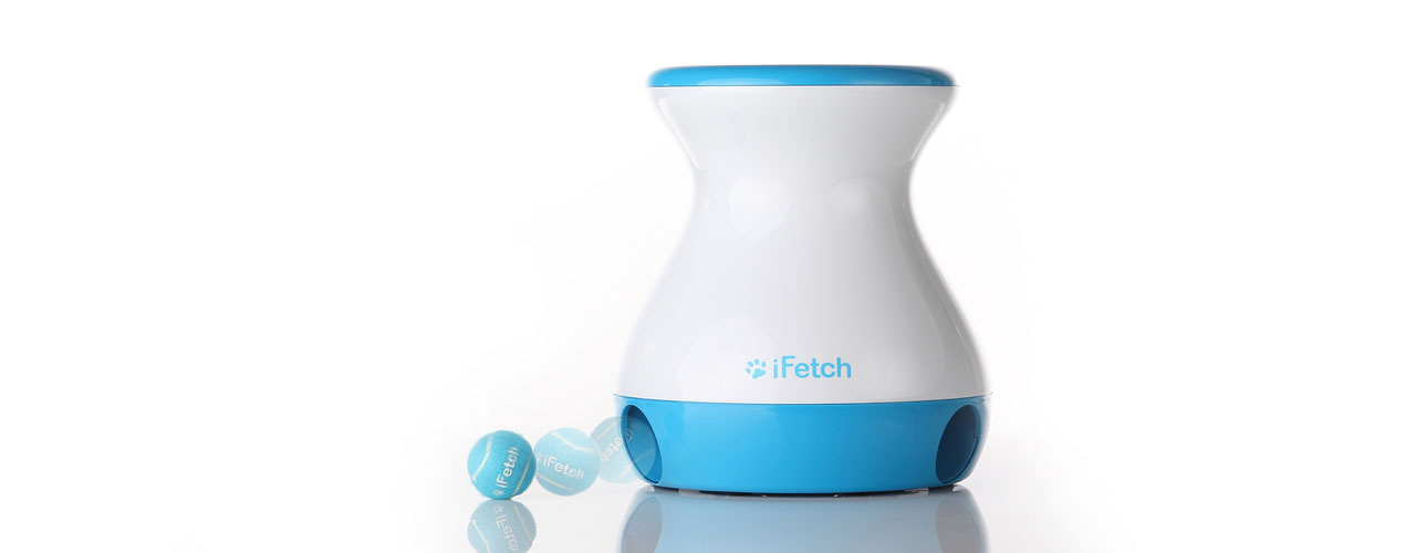 The iFetch Frenzy with a ball rolling out of one of the dispenser holes, while sitting on a reflective table. 